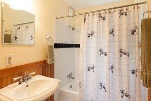 Un baño con lavamanos, espejo, ducha y perchero para toallas.