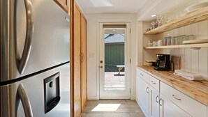 Eine Küche mit einem Edelstahlkühlschrank, Holzschränken, einer weißen Arbeitsplatte und einer Tür zu einem Außenbereich.