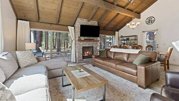 A cozy living room with a stone fireplace, leather sofa, and a flat-screen TV mounted on the wall.