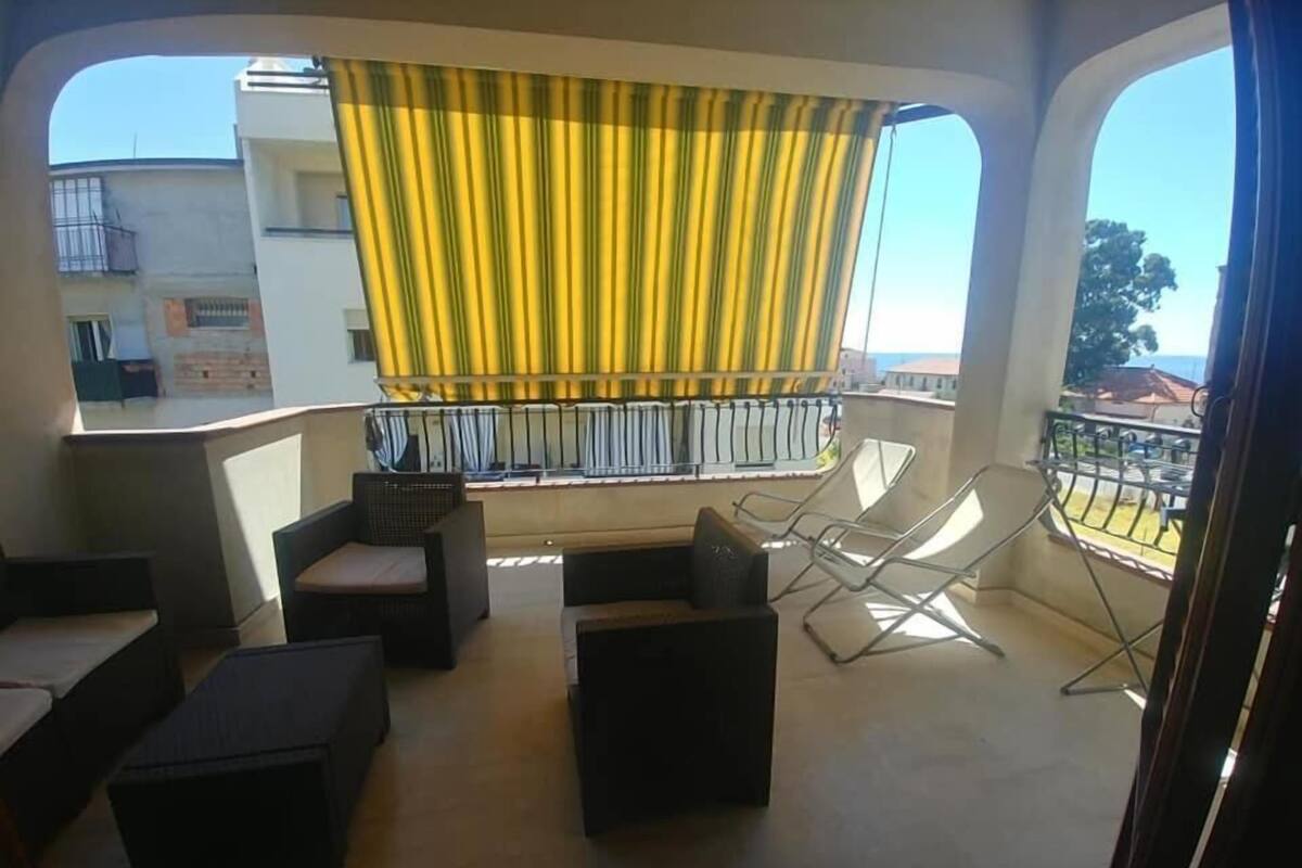 Un balcon avec des sièges pour l’extérieur, un rideau jaune et une vue sur les immeubles.