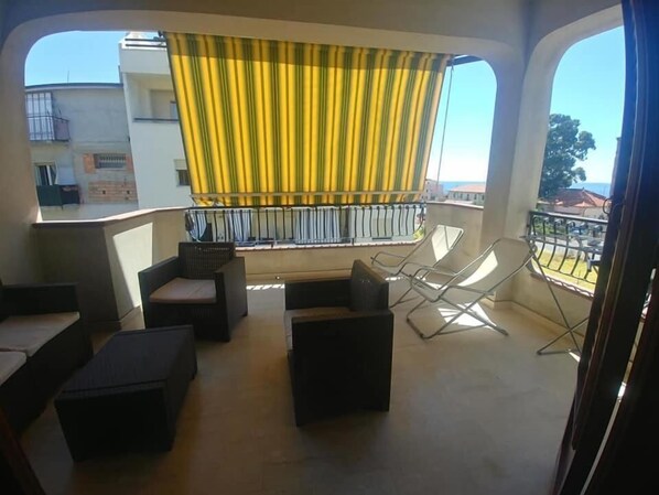 Un balcon avec des sièges pour l’extérieur, un rideau jaune et une vue sur les immeubles.