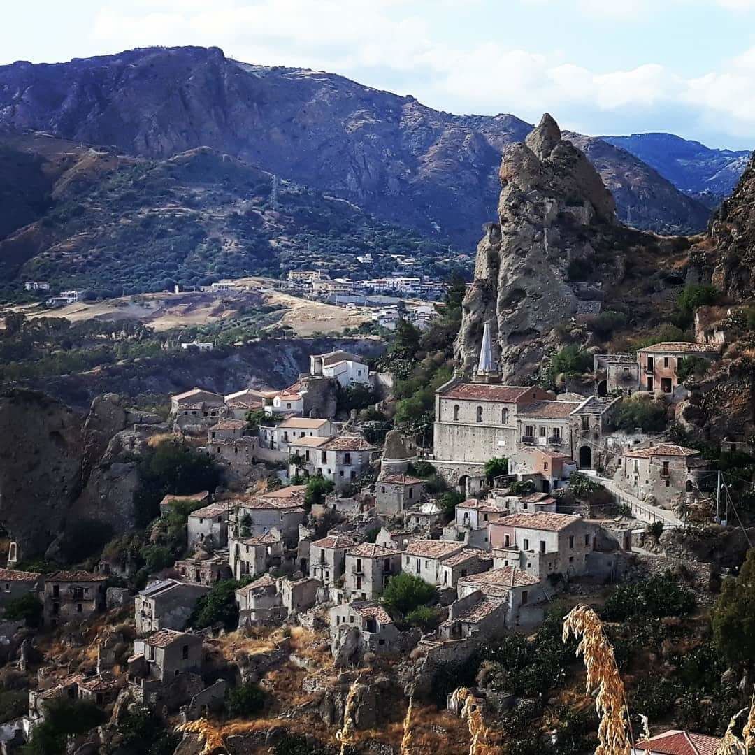 A mountainous village with historic stone buildings, a prominent church, and a rocky peak.