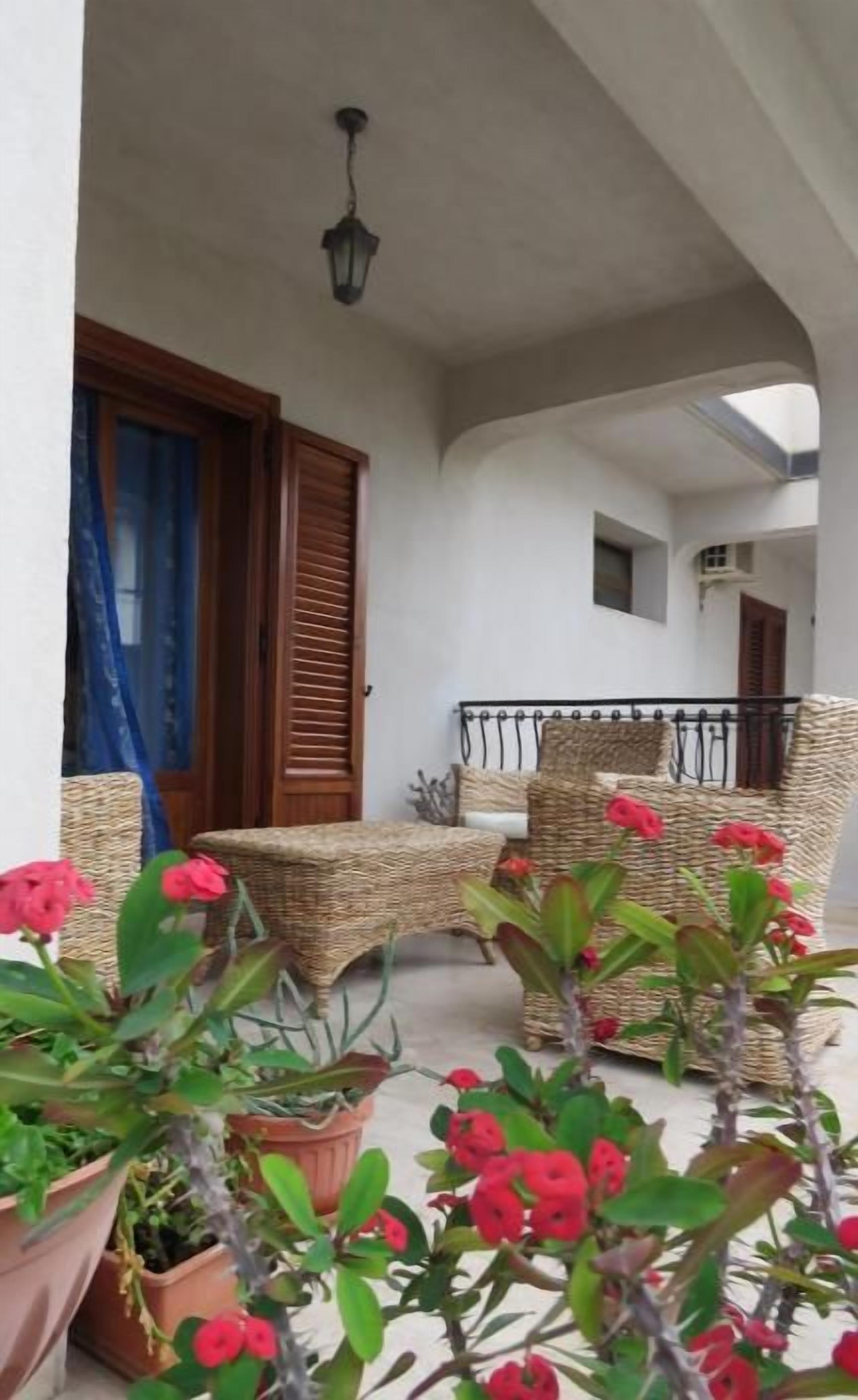 A covered outdoor seating area with wicker furniture, potted plants, and a small balcony.