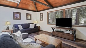 A living room with a wooden ceiling, a sofa, a coffee table, a TV on a stand, and framed pictures on the wall. - 3 Killdeer Lane Pet Friendly Home 3 Minutes Walk from SHARC by RedAwning (Bend)