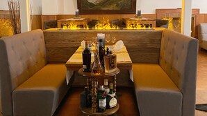 A restaurant with a wooden table, two cushioned seating areas, a central table with bottles, and a painting on the wall. - Hotel du Glacier (Fiesch)