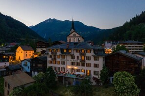 A hotel with a prominent church spire, surrounded by mountains and other buildings. - Hotel du Glacier (Fiesch)