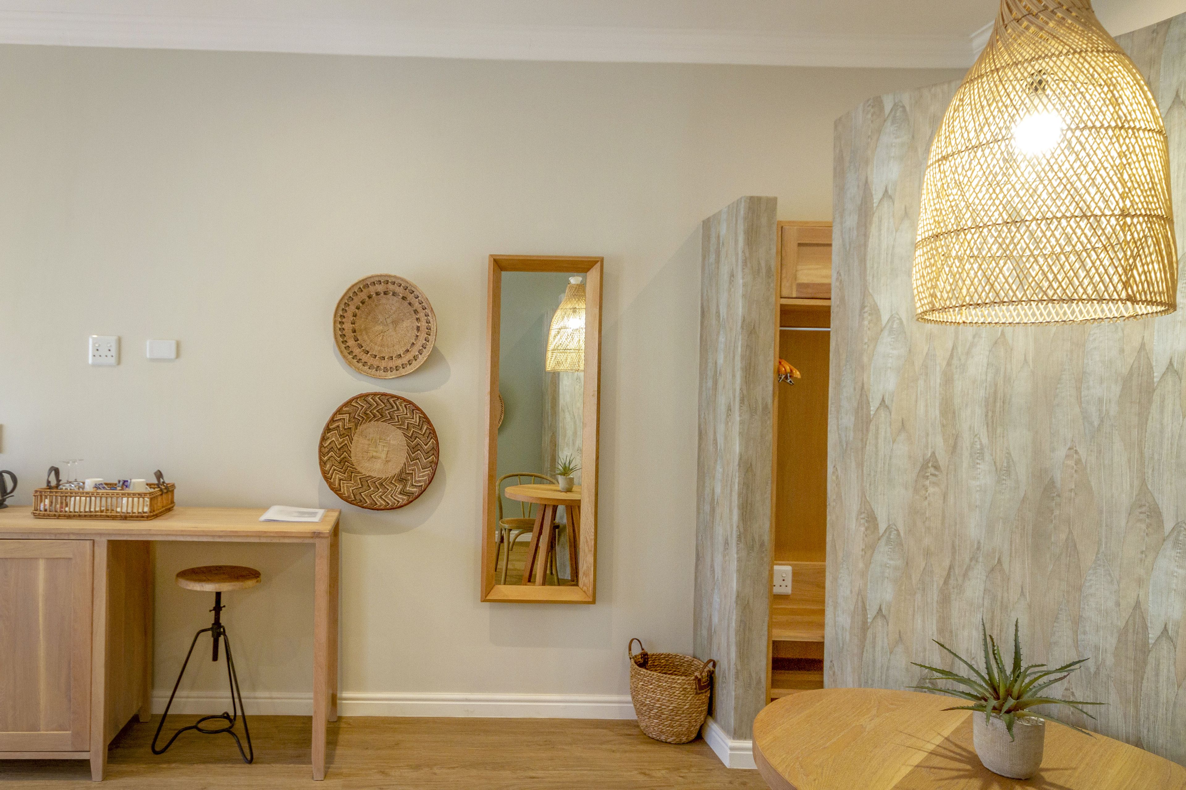 A room with a wooden desk, a stool, a mirror, and a hanging light fixture.