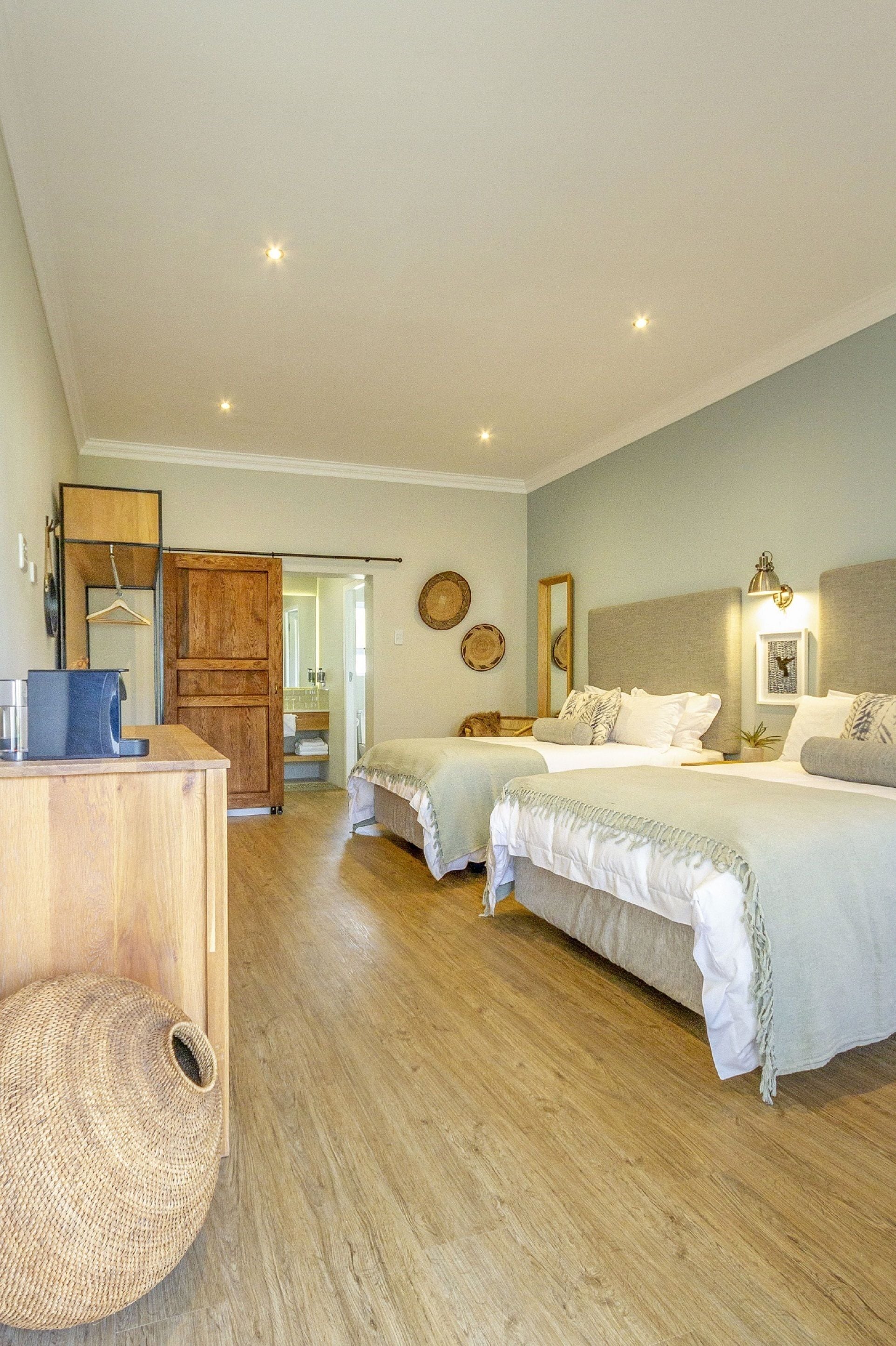 A bedroom with two beds, wooden flooring, a desk, and a wardrobe.