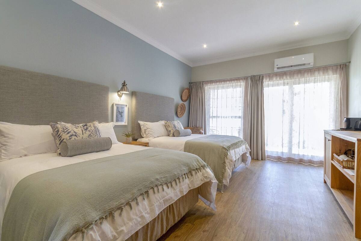 Una habitación de hotel con dos camas, una mesita de noche, un equipo de aire acondicionado y un armario de madera.