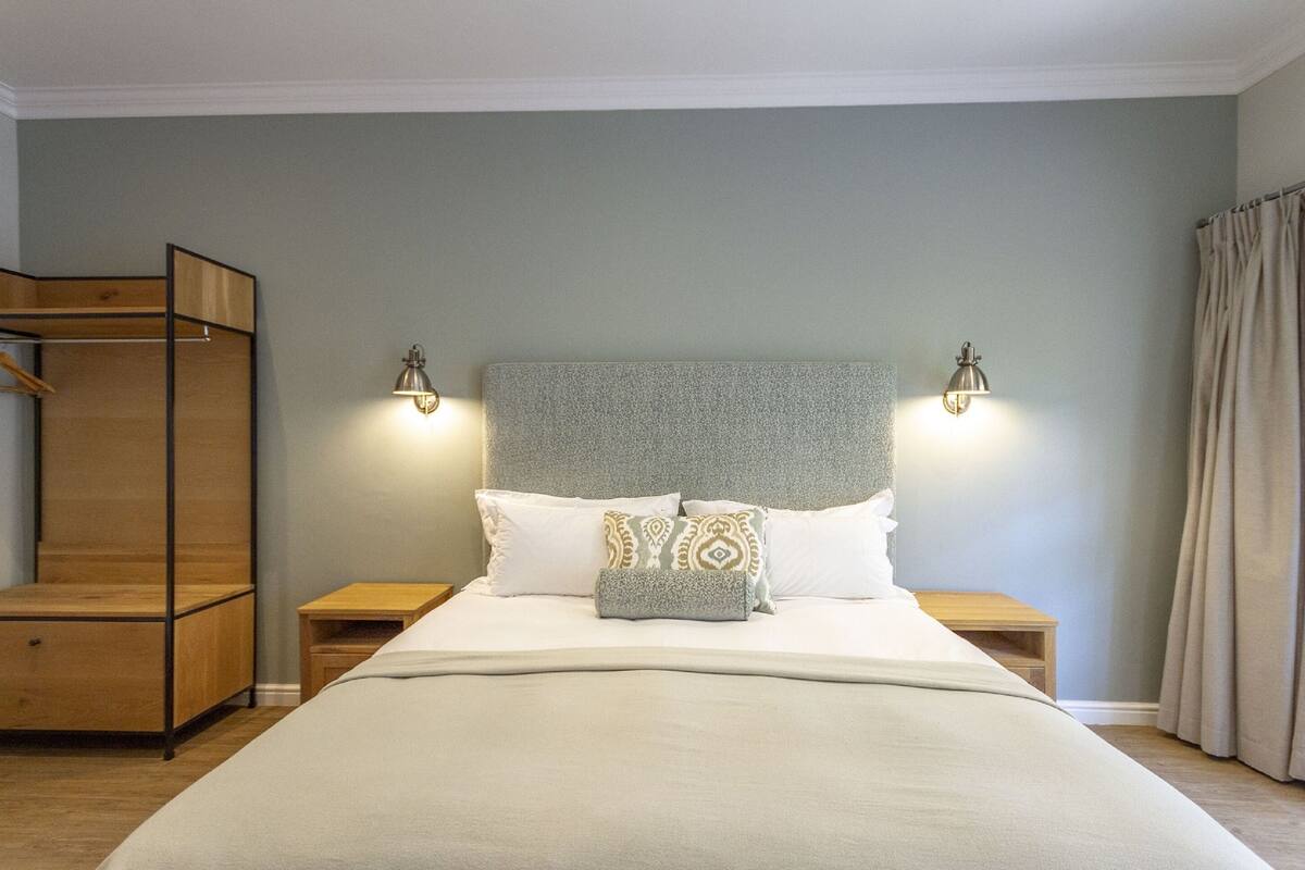 Un dormitorio ordenado con una cama grande, dos mesitas de noche, un armario de madera y dos lámparas de pared.