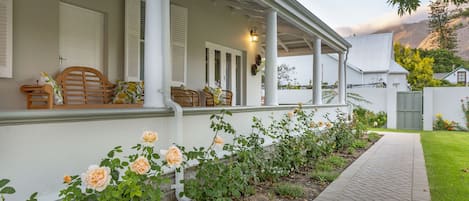 A covered porch with wicker furniture, a pathway, and a row of roses.