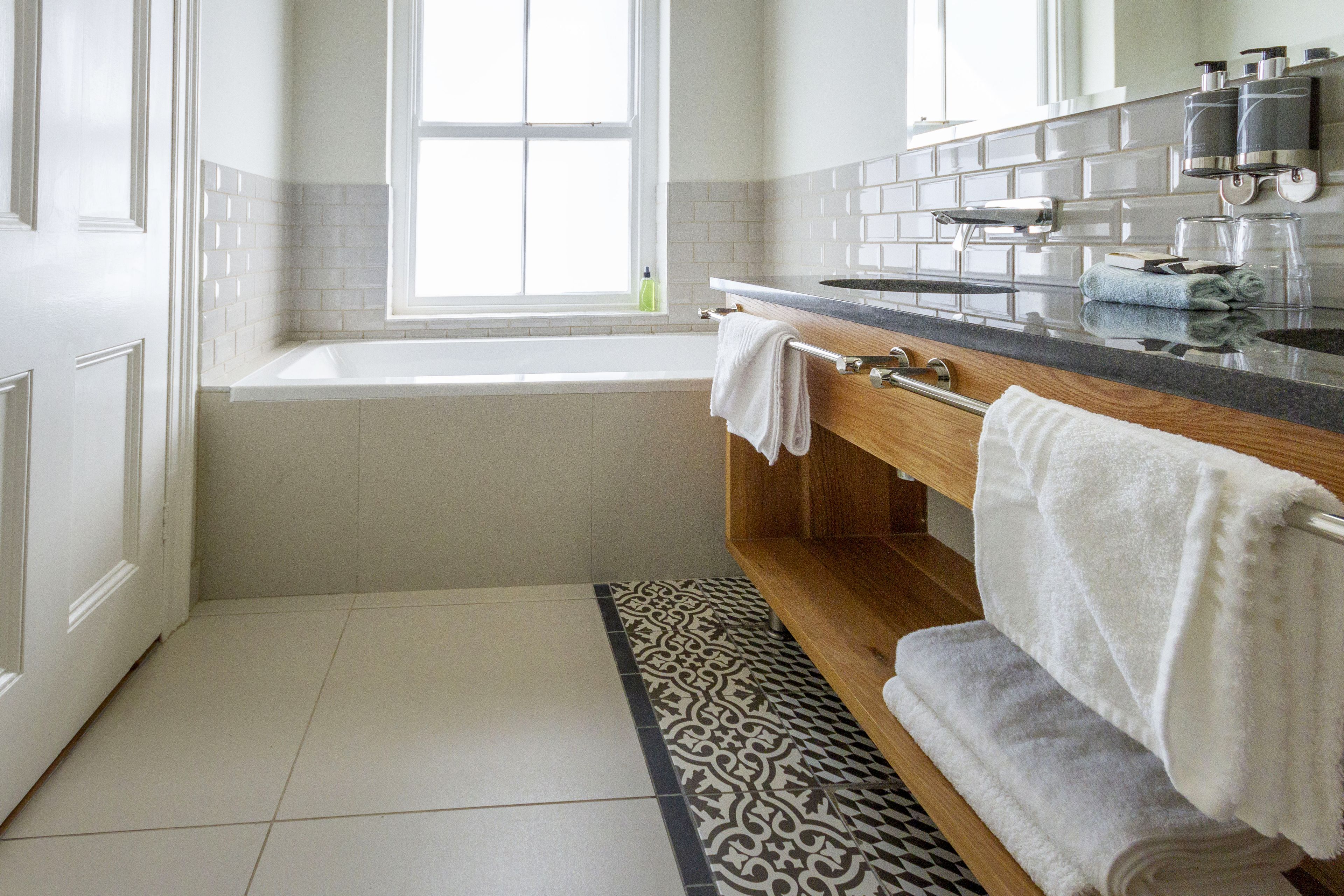 A modern bathroom with a bathtub, a wooden vanity, and a patterned rug.