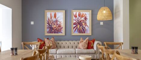 A dining area with a wooden table, chairs, a sofa, and two framed artworks on the wall.