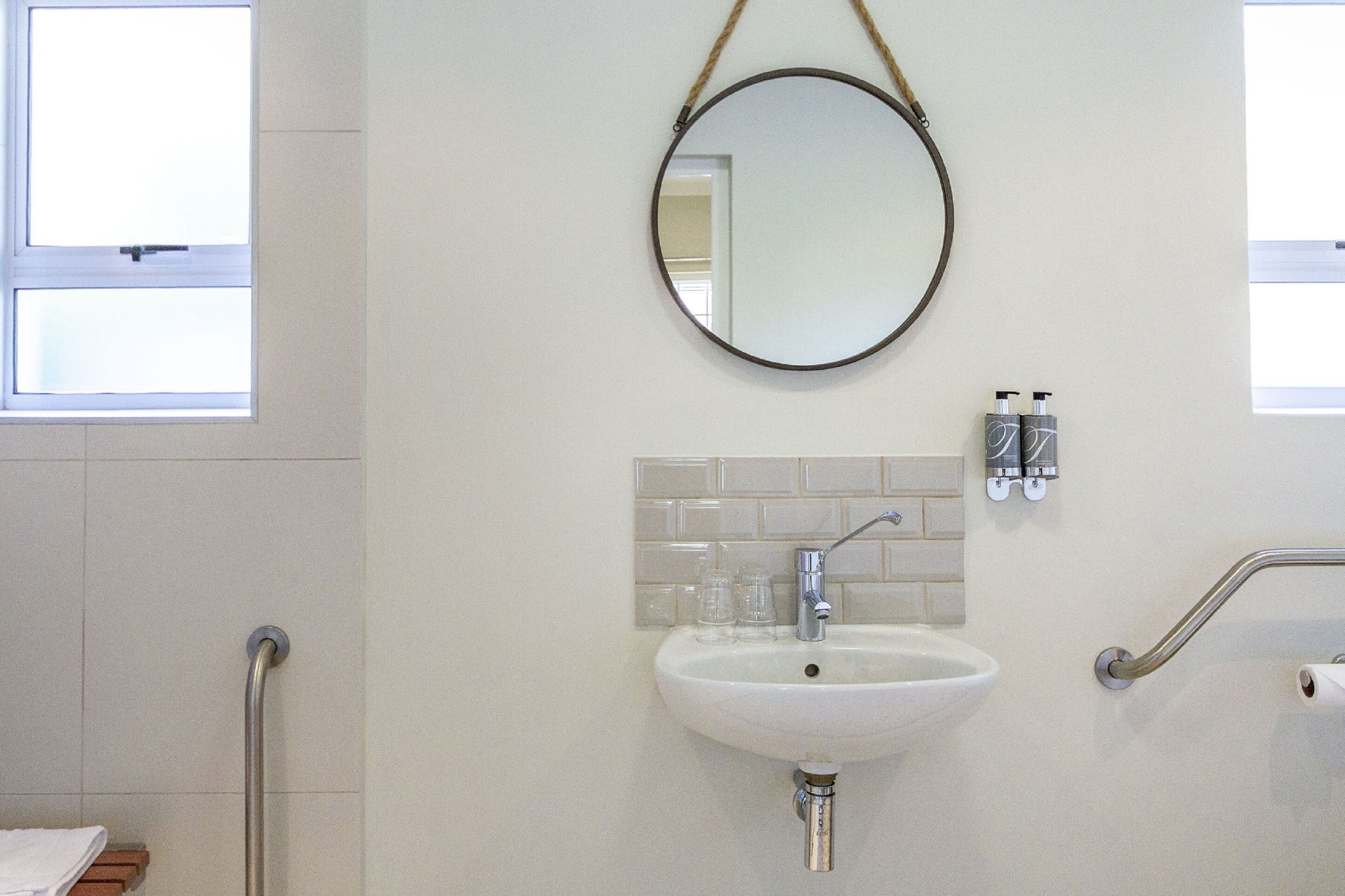 Une salle de bain avec un lavabo blanc, un miroir rond et une fenêtre.