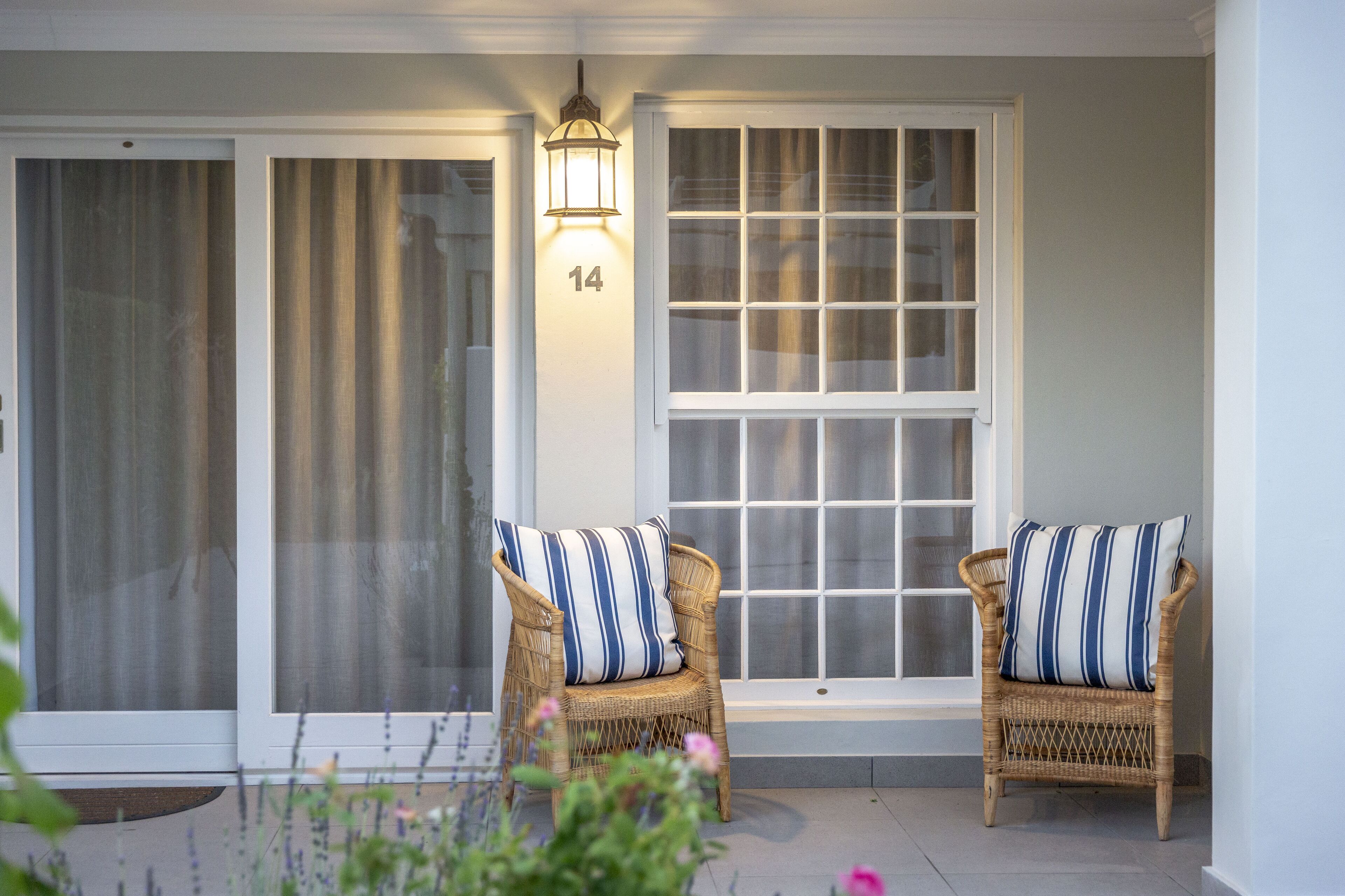 A porch with two wicker chairs, a number 14 sign, and a lantern.