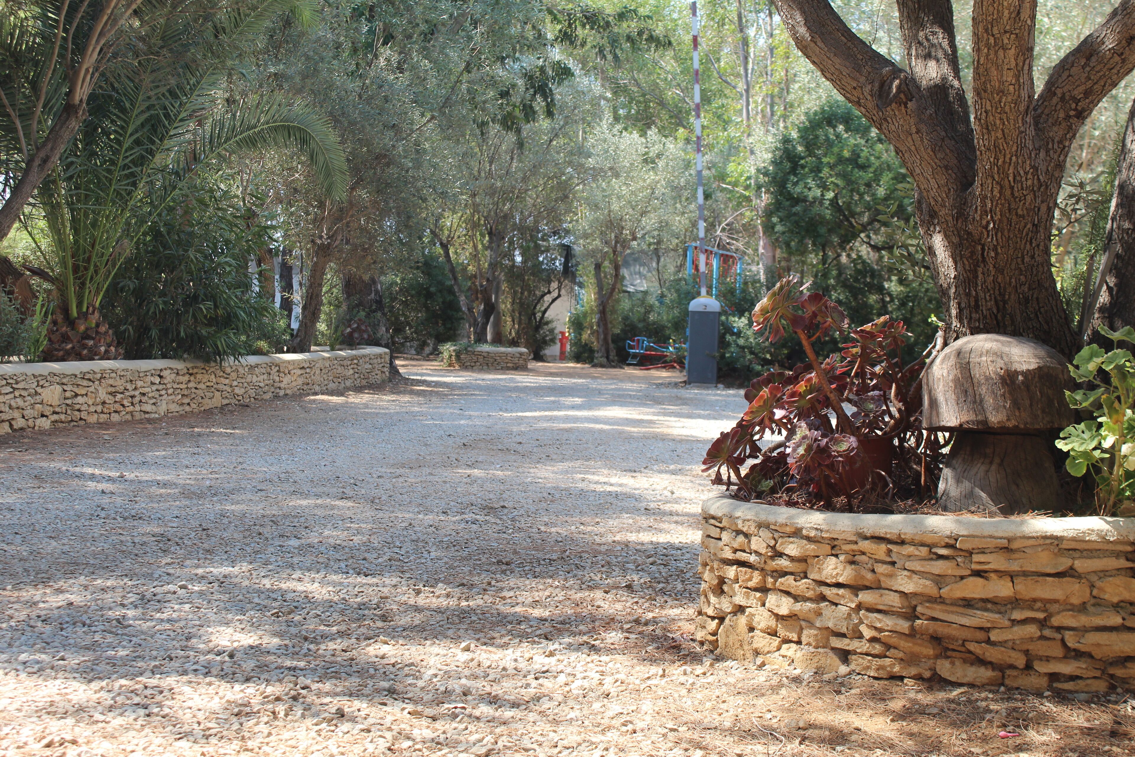 A pathway lined with stone walls and trees, leading to a playground area.