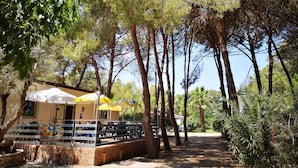 A restaurant with outdoor seating, surrounded by tall trees and a stone wall.