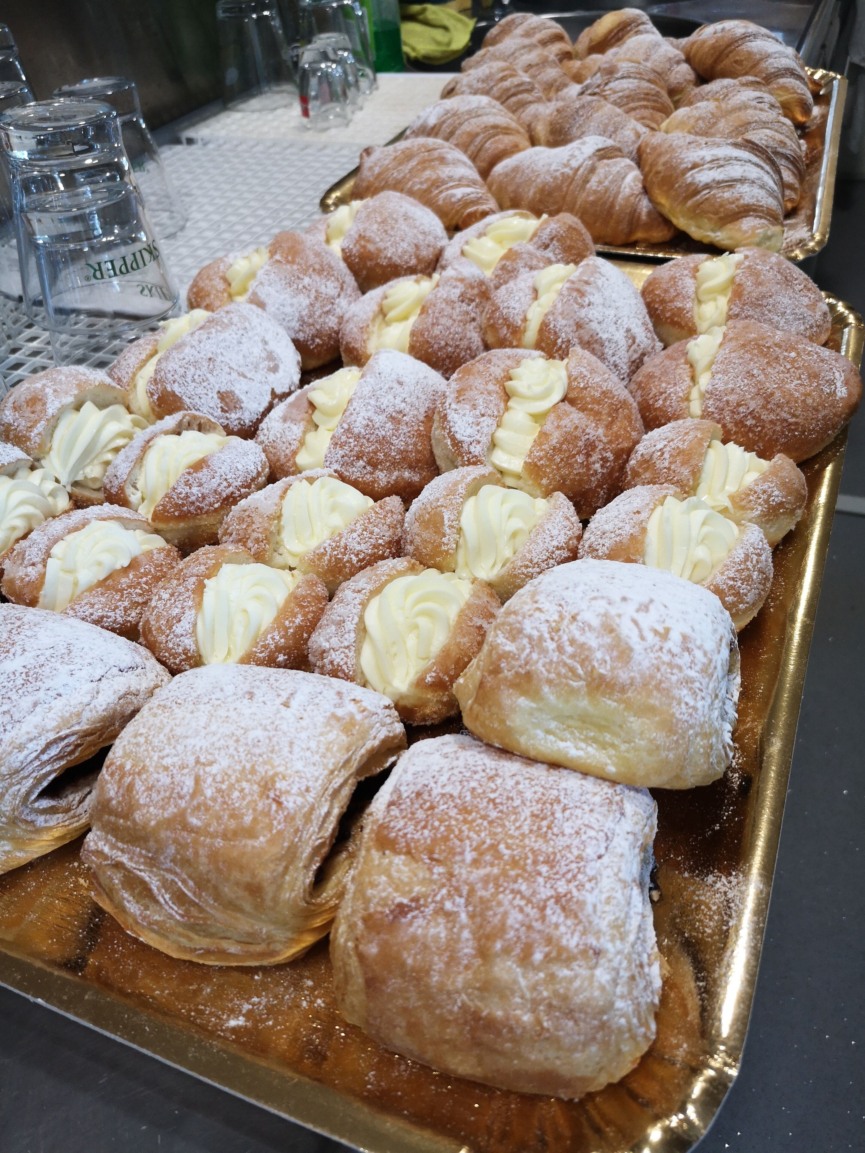 A tray of assorted pastries including cream puffs and croissants, dusted with powdered sugar.