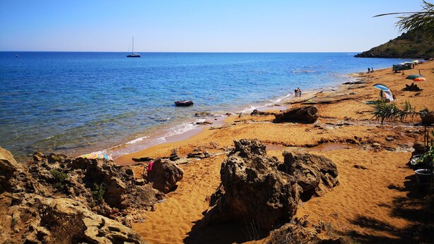 A beach with clear blue water, a sandy shore, and a few people.