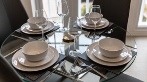 Una mesa de comedor dispuesta con platos, tazones y copas de vino, rodeada de sillas negras.