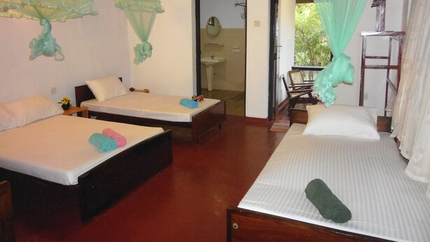 A room with two beds, a wooden ceiling, a sink, and a view of greenery outside.
