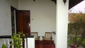 A porch with two wooden chairs, a potted plant, and a red floor.