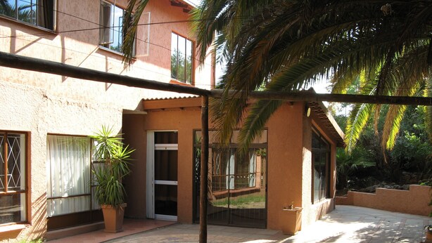 A courtyard with a paved walkway, a glass door entrance, and a potted plant. - Johannesburg Boarding Hostel (Randburg)
