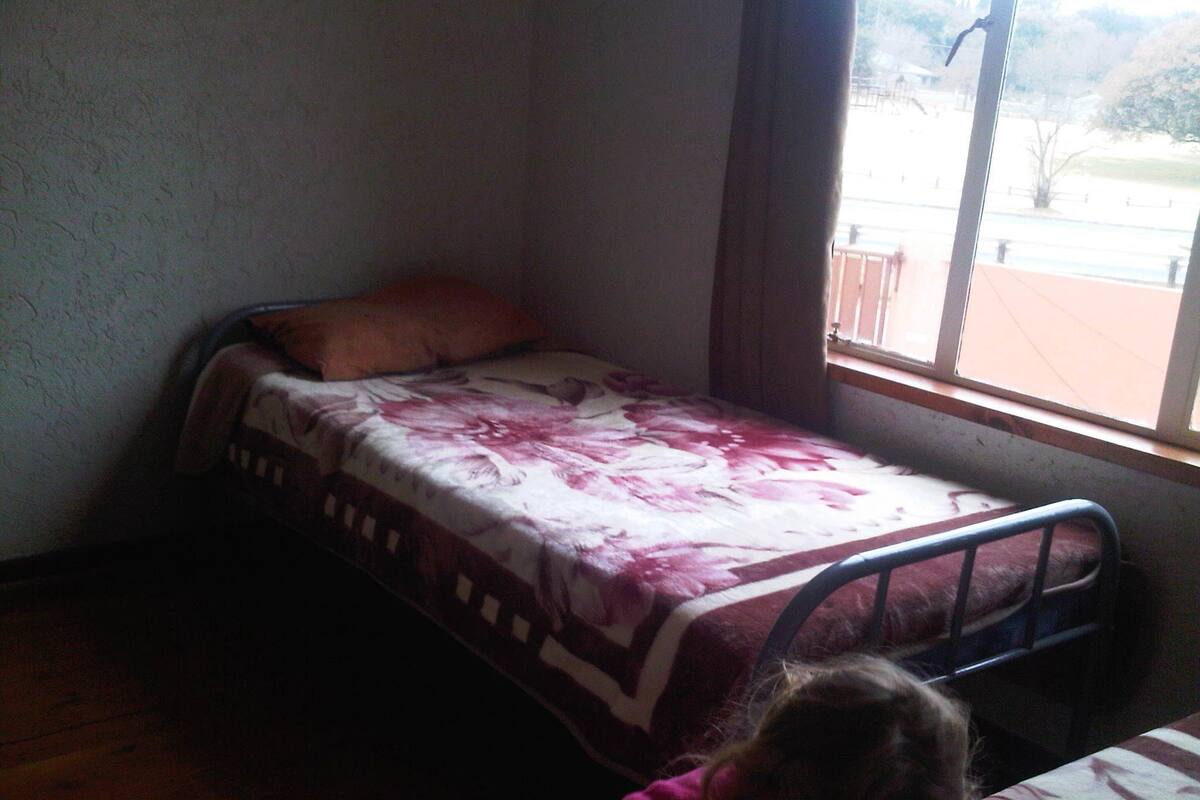 A small, single-bed room with a window, a wooden floor, and a floral bedspread.
