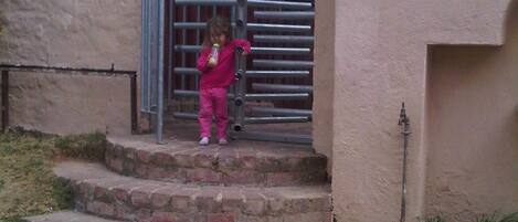 A child in pink clothing standing on a set of stone steps leading to a metal gate.