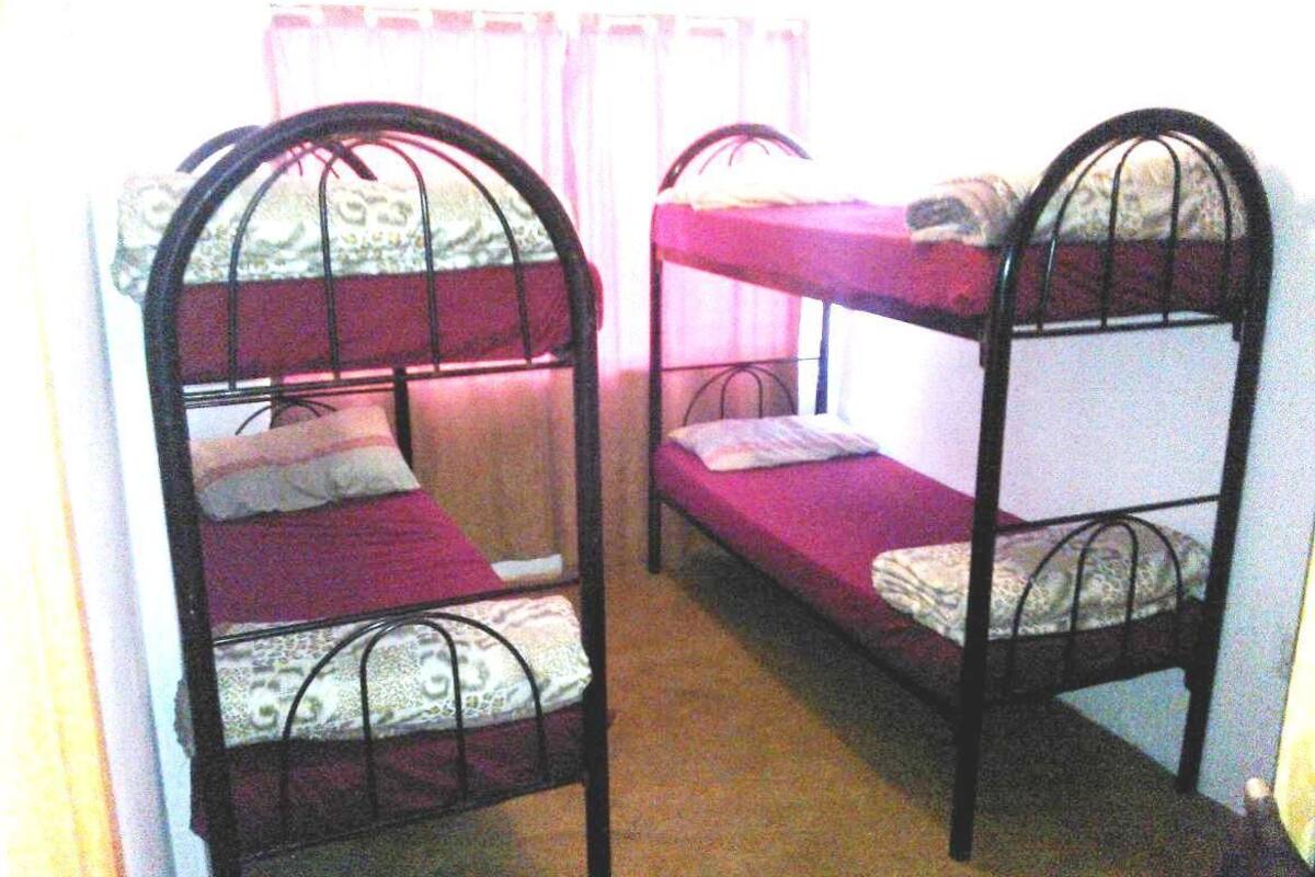 Two bunk beds with metal frames and purple bedding, arranged in a small room with a window and curtains.