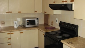 A kitchen with white cabinets, a microwave, a stove, and a red pot on the counter. - Johannesburg Boarding Hostel (Randburg)