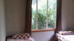A bedroom with two beds, a window with curtains, and a view of greenery outside. - Johannesburg Boarding Hostel (Randburg)