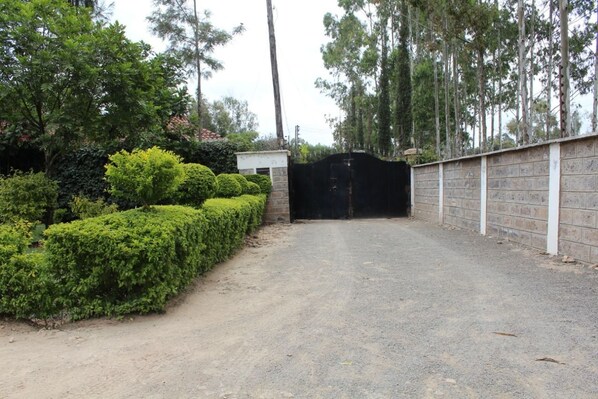 Un camino de entrada con portón que conduce a un edificio con muro de ladrillo y una pequeña construcción.