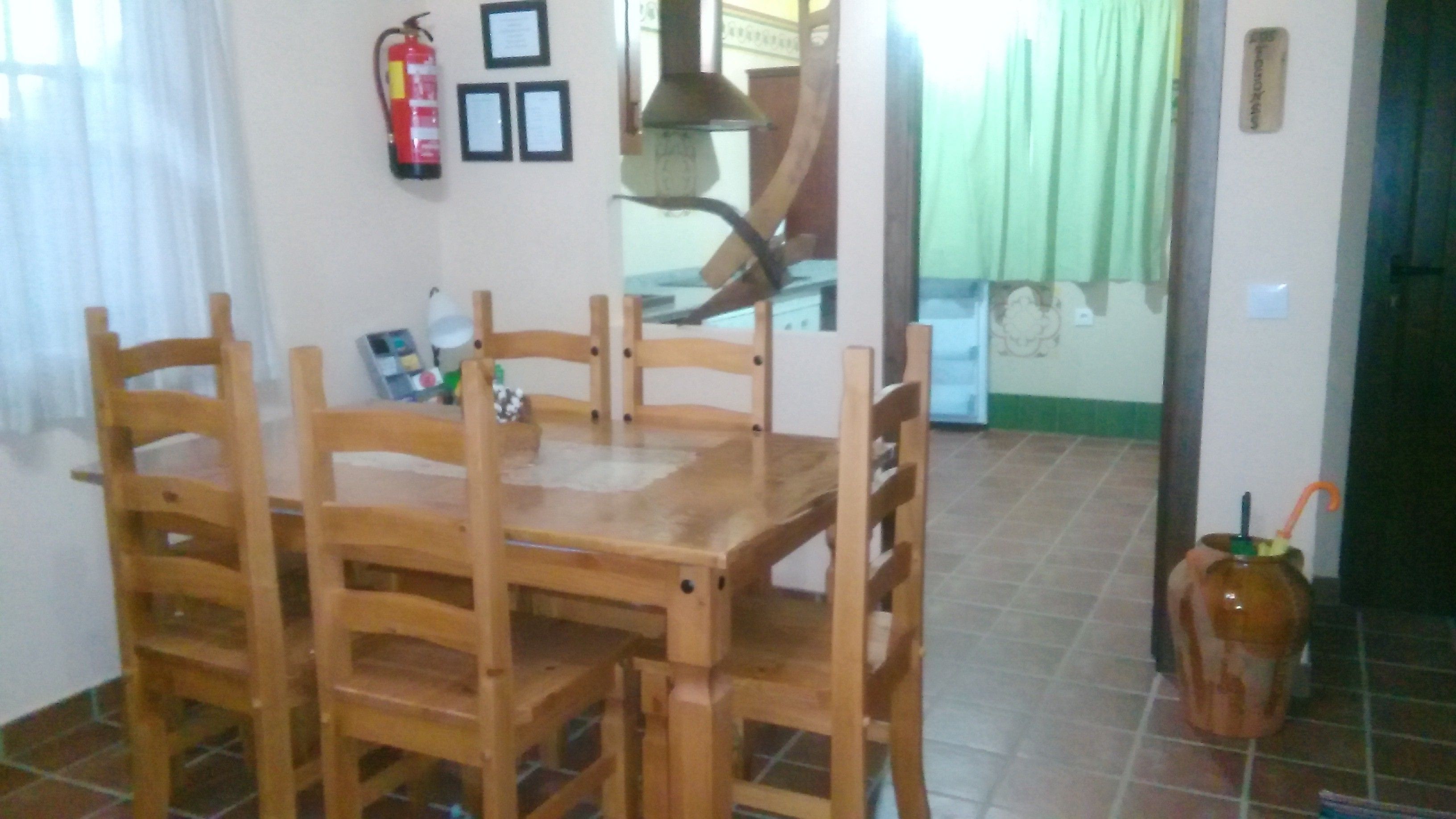 Un comedor con una mesa y sillas de madera, un extintor, certificados enmarcados en la pared y suelo de baldosas.