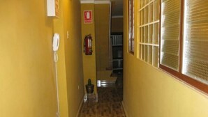 Un pasillo estrecho con paredes amarillas y suelo de madera. Se observa un extintor de incendios en la pared y un teléfono a la izquierda.