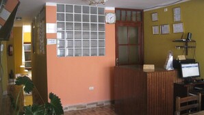 Zona de recepción con mostrador de check-in, un reloj y una pared con certificados enmarcados.