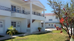 A two-story white building with a balcony, a staircase, and a small garden area with a palm tree and a potted plant. - Deluxe Apartment with 2 Bedrooms B - 2 Br apts (Albufeira)