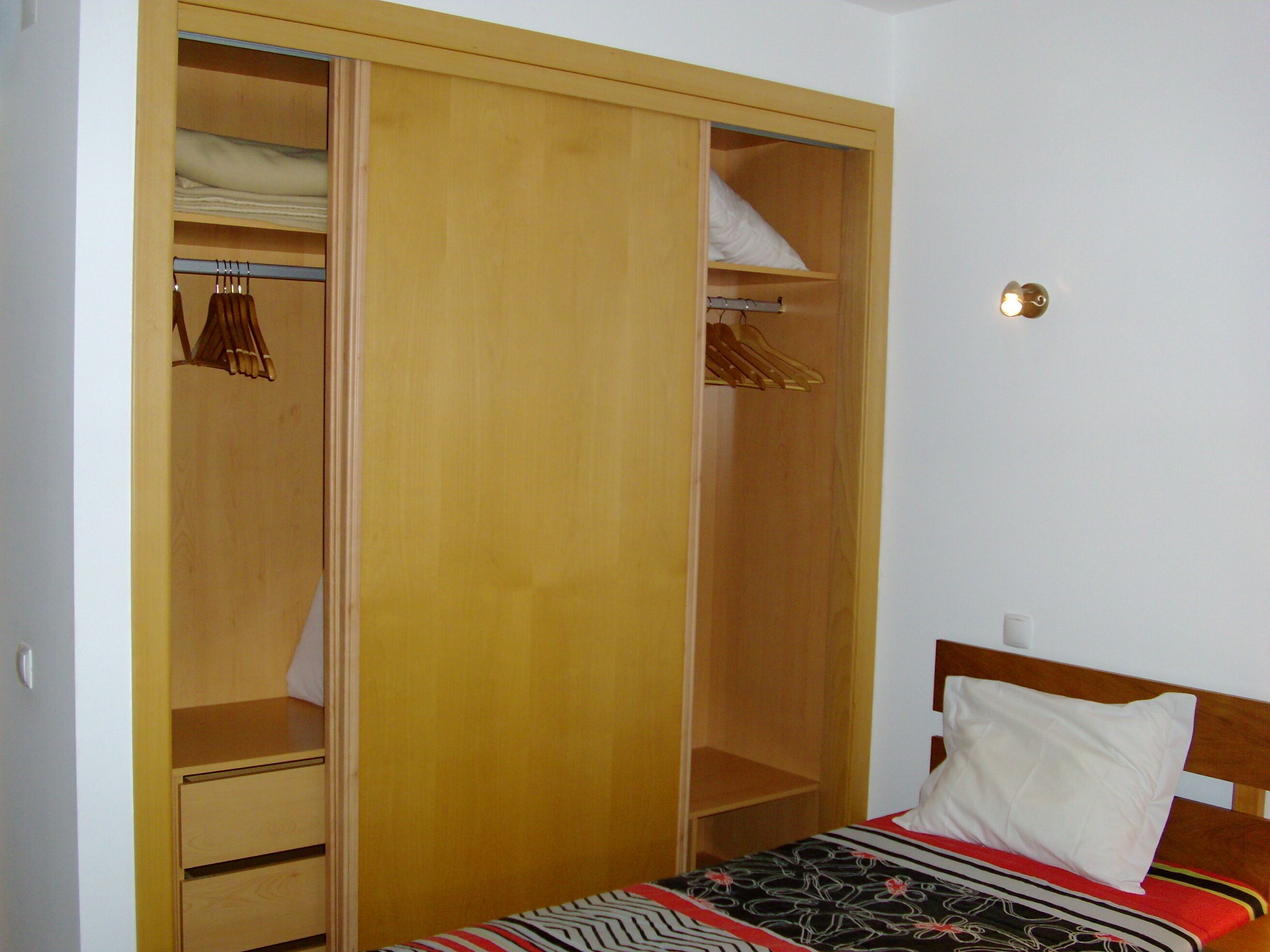 Una camera da letto con un letto, un armadio in legno con scomparti multipli e un comodino.