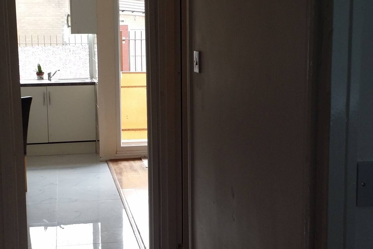Un couloir dallé qui mène à une cuisine équipée de meubles de rangement et dotée d’une fenêtre.