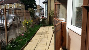 A narrow pathway leading to a residential area with a gated entrance, a small garden with flowers, and a parked car. - Stunning Apartment In London Tottenham (London)
