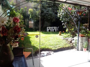 A glass-enclosed patio with a garden view, outdoor furniture, and a variety of plants. - Samadri Hospedaje (Arequipa)