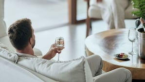 Un hombre y una mujer sentados en un sofá blanco y una silla blanca, respectivamente, en una habitación luminosa con un ventanal grande.