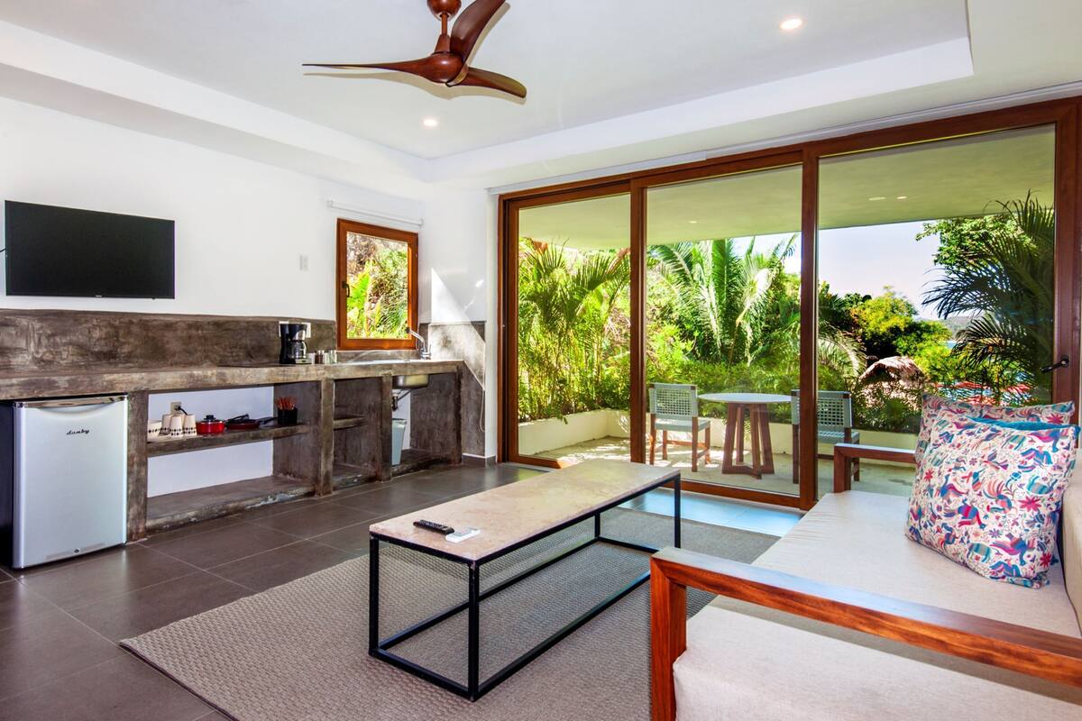 Una cocina moderna con refrigerador empotrado, cafetera y un amplio ventanal con vistas a un jardín.
