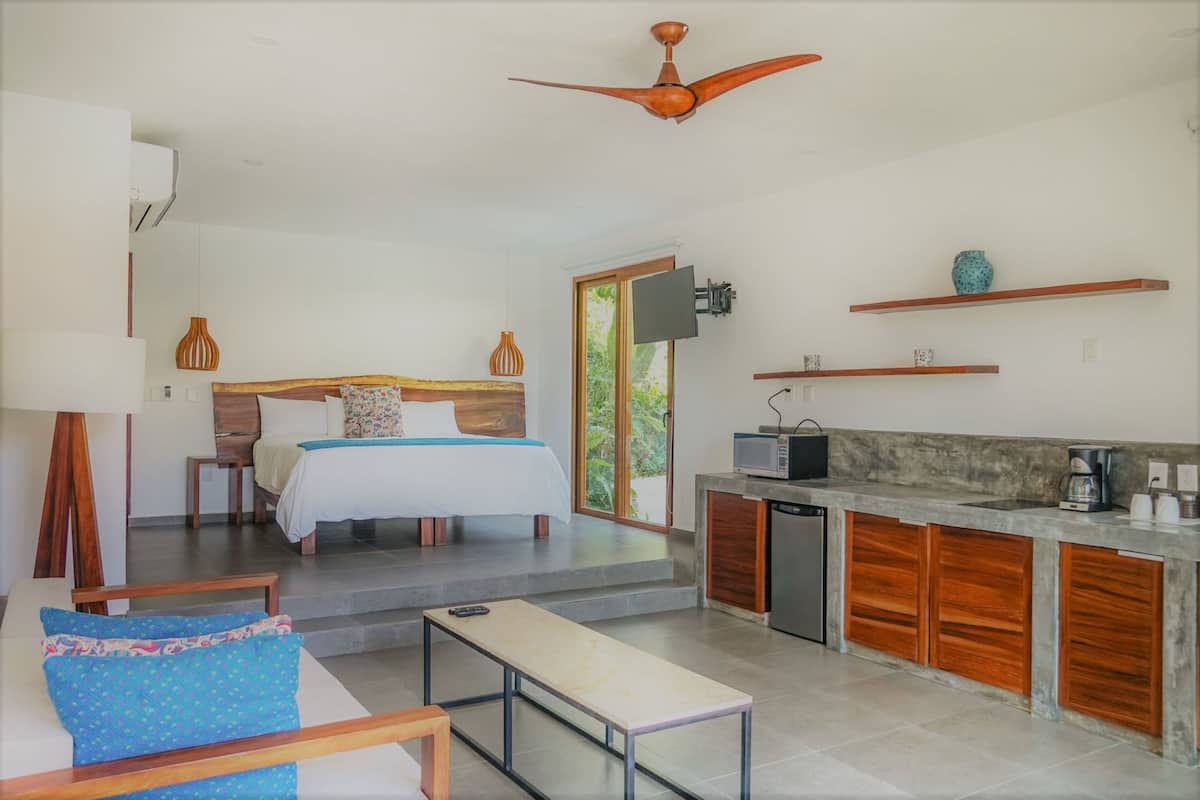 Una habitación de hotel moderna con cama, escritorio, banca, kitchenette y ventilador de techo.