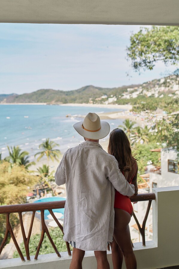 A couple overlooking a beach from a balcony with a view of the sea and palm trees.
