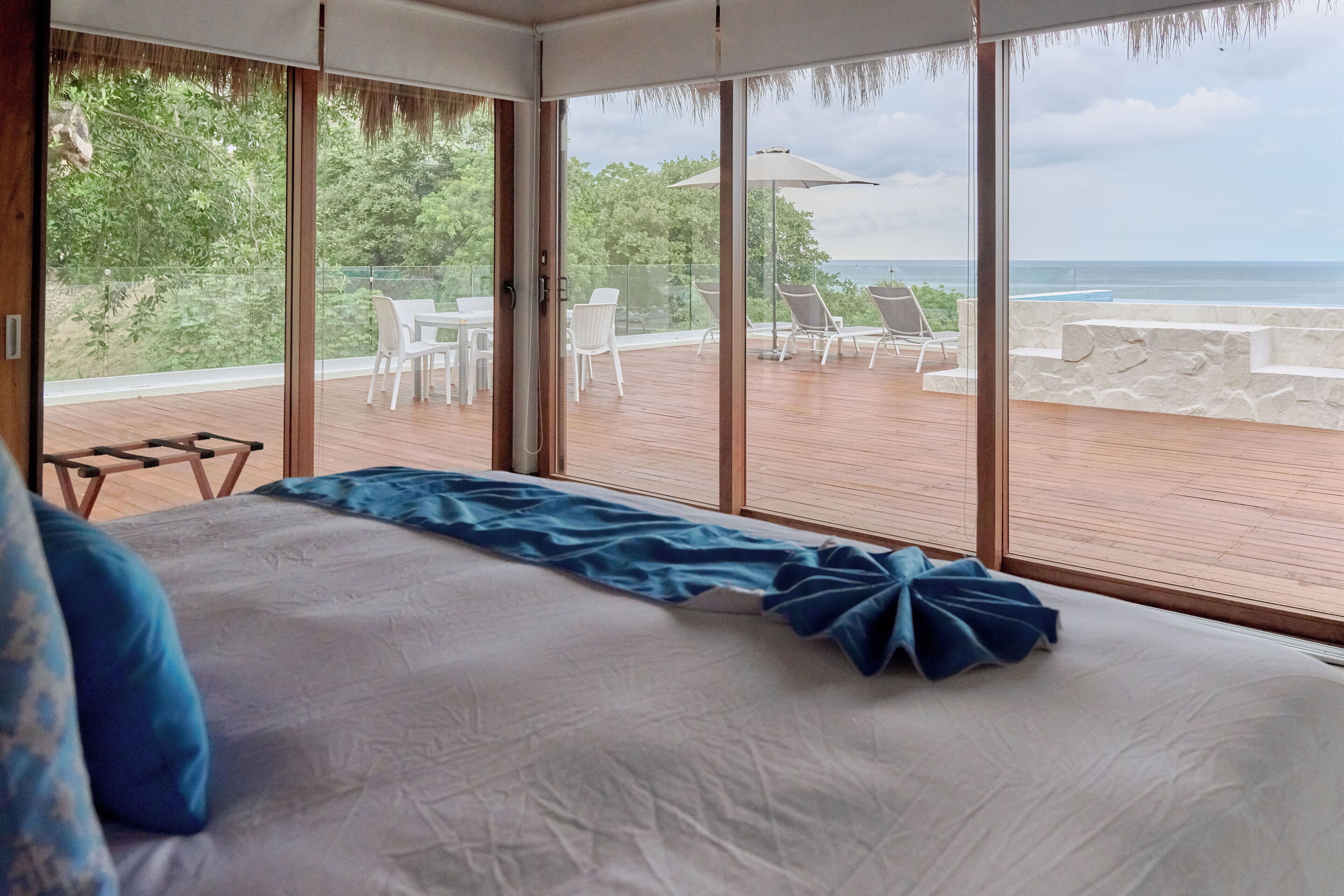 Un dormitorio con una cama grande, vistas al océano y un balcón con mobiliario de exterior.