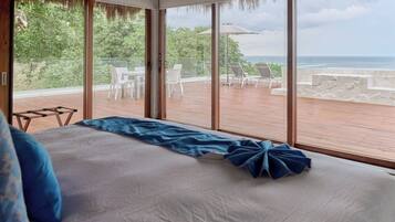 Un dormitorio con una cama grande, vistas al océano y un balcón con mobiliario de exterior.