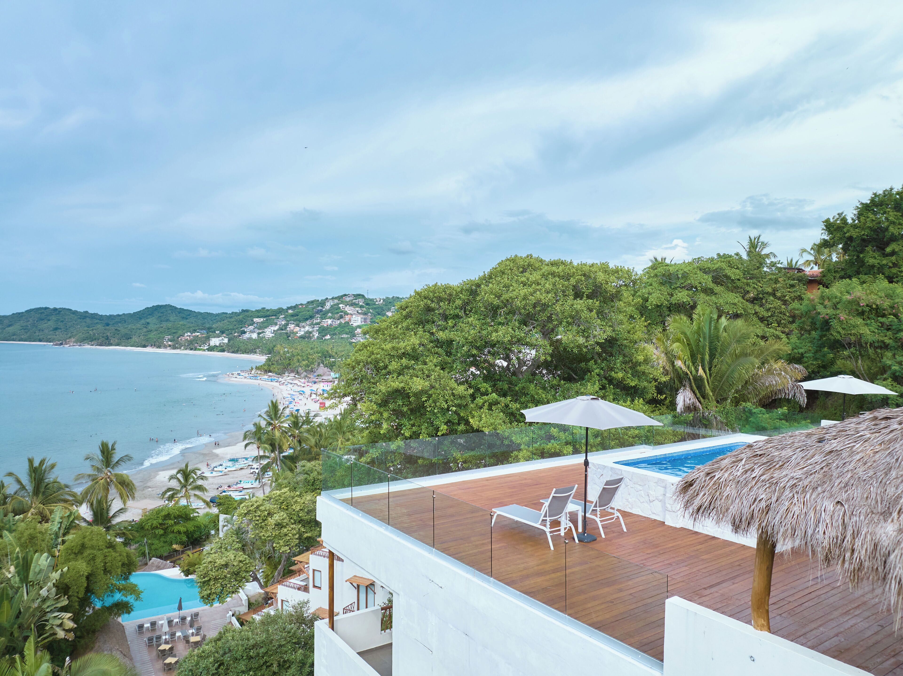 A poolside area with a wooden deck, lounge chairs, and a thatched umbrella.
