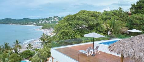 A poolside area with a wooden deck, lounge chairs, and a thatched umbrella.
