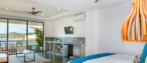 Habitación de hotel moderna con una cama grande, zona de comedor con vistas, cocina y dos ventiladores de techo.